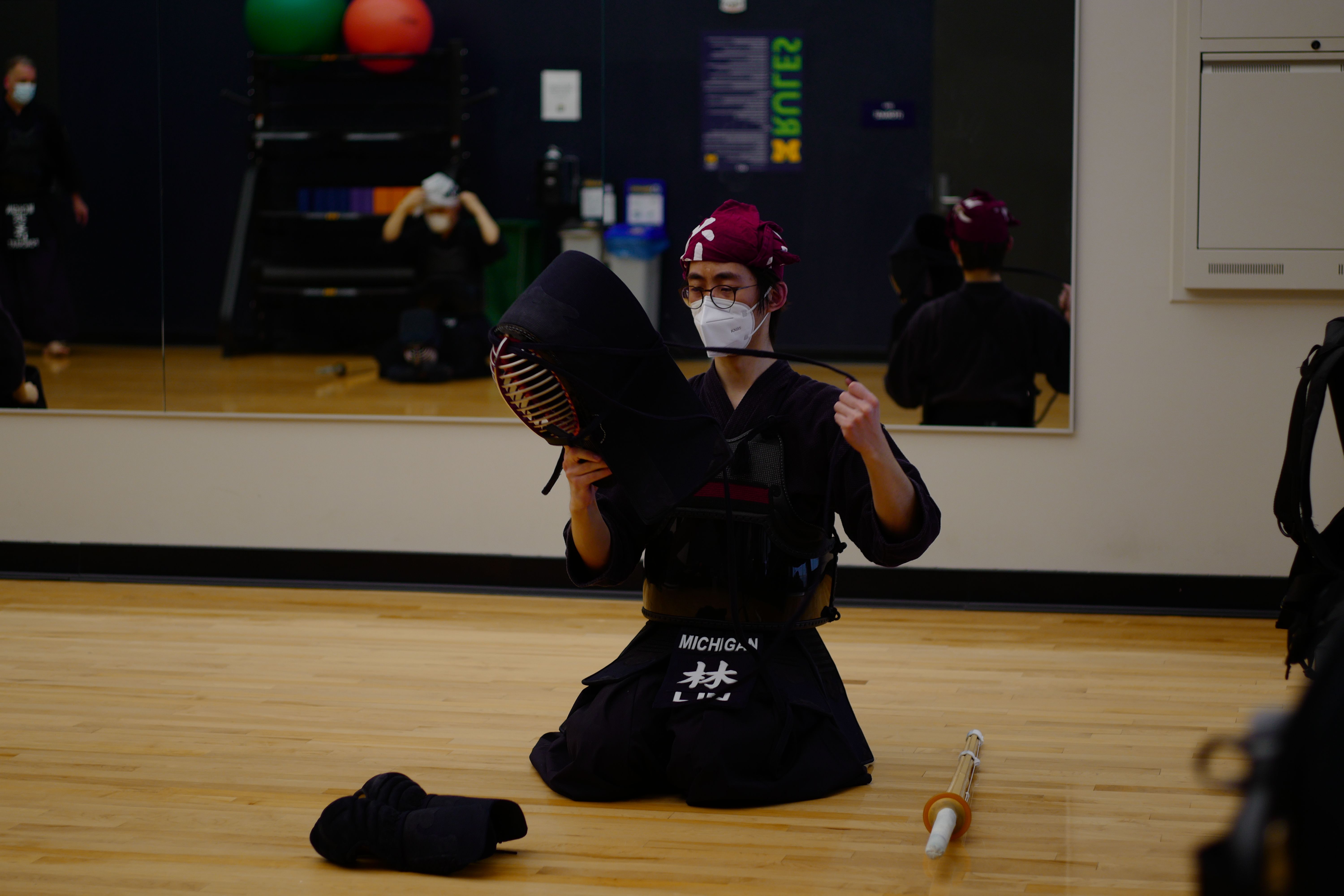 A club member sitting with most of their armor on, putting on the helmet.